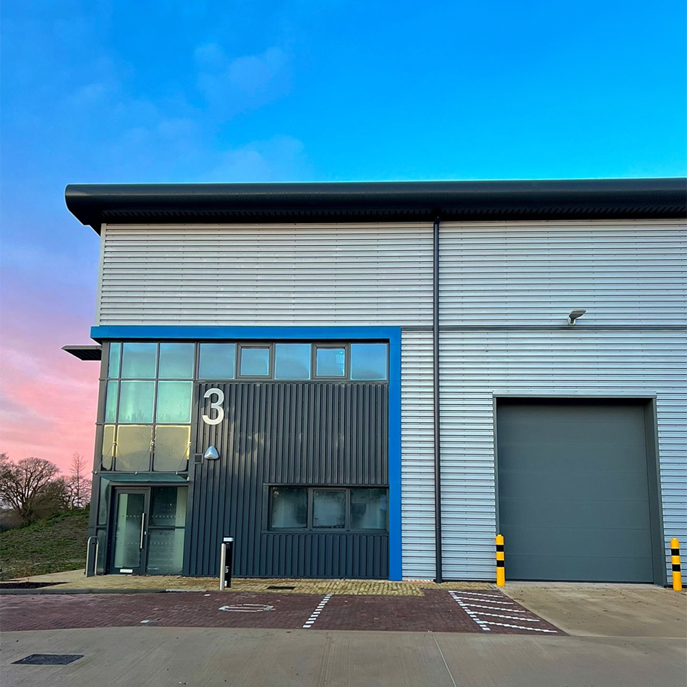 Evergy’s modern head office and warehouse in Thame, a grey and blue industrial building with large windows and a sunset sky.